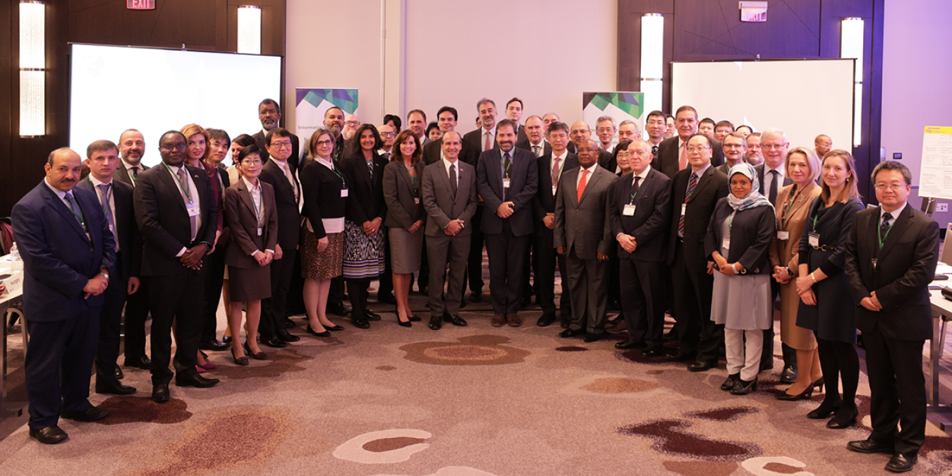 Group of 24 people standing in rows facing the camera, at the head of a conference room.