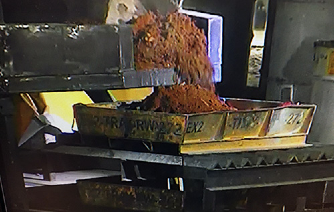 An excavator empties the contents of a sludge drum into a sorting tray at the Accelerated Retrieval Project VII facility.