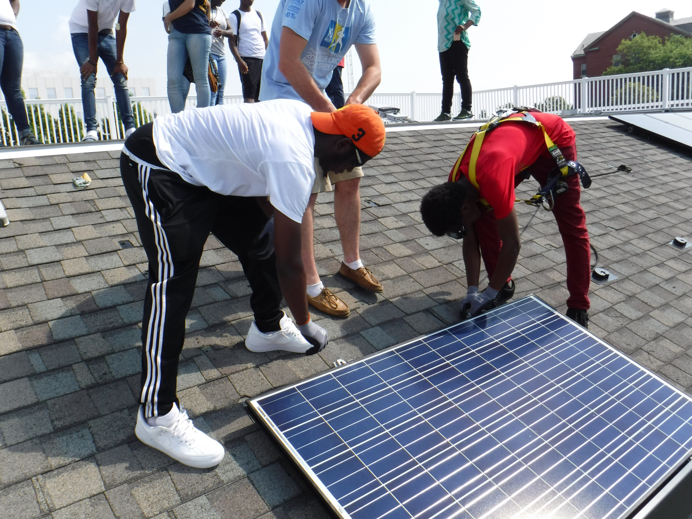 High school students practice installing solar panels on a mock roof