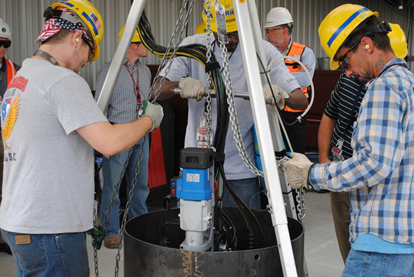 Workers test a modified cutting tool in a mock demonstration before using it to modify storage positions for waste canisters inside the Glass Waste Storage Building 1.