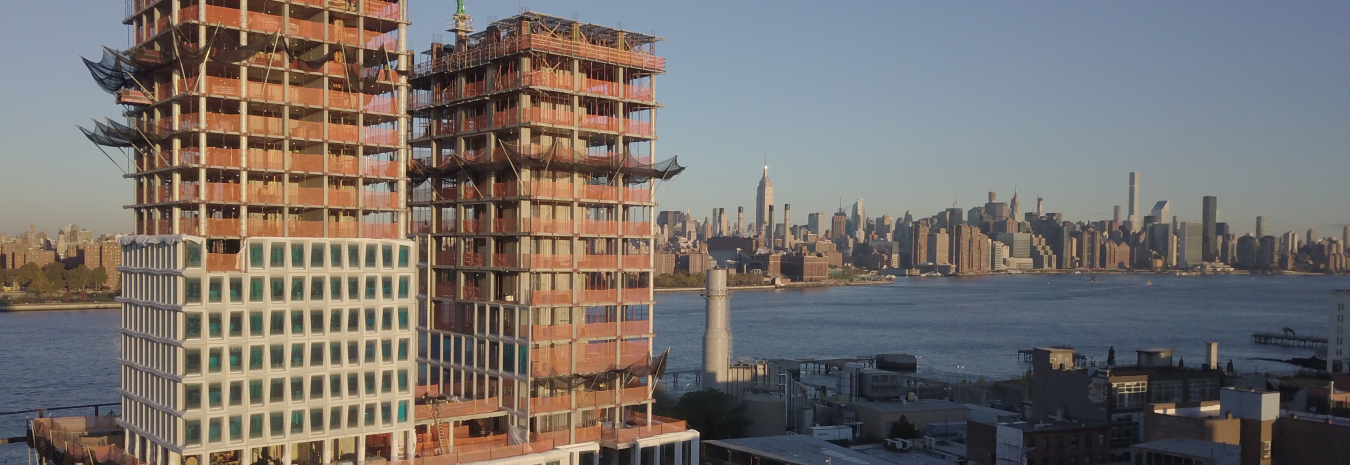The skyline of New York City in daytime in the background, with a tall building complex under construction in the foreground. Image from ORNL.gov.
