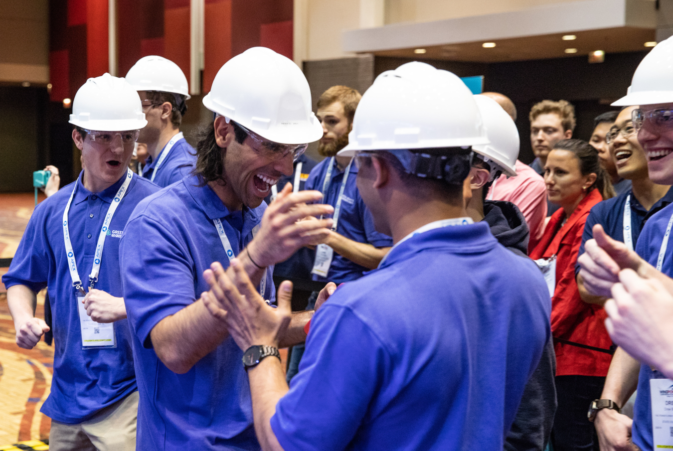 A group of young men in hard hats and safety goggles give each other high-fives.