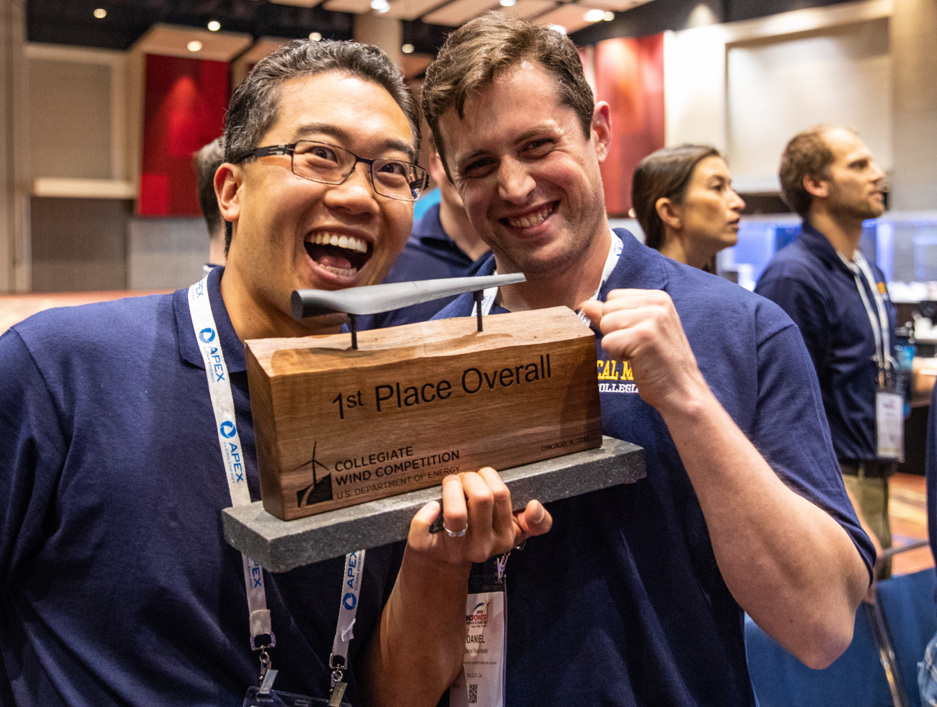 Two young men smile while holding up a 1st place Collegiate Wind Competition trophy.