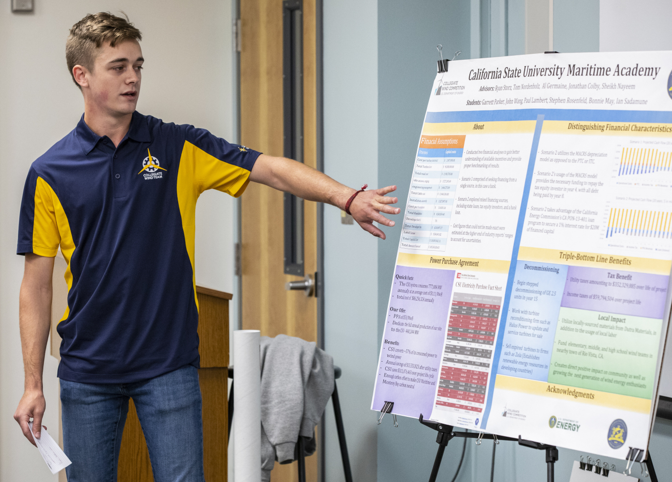 A young man gestures toward a presentation poster.