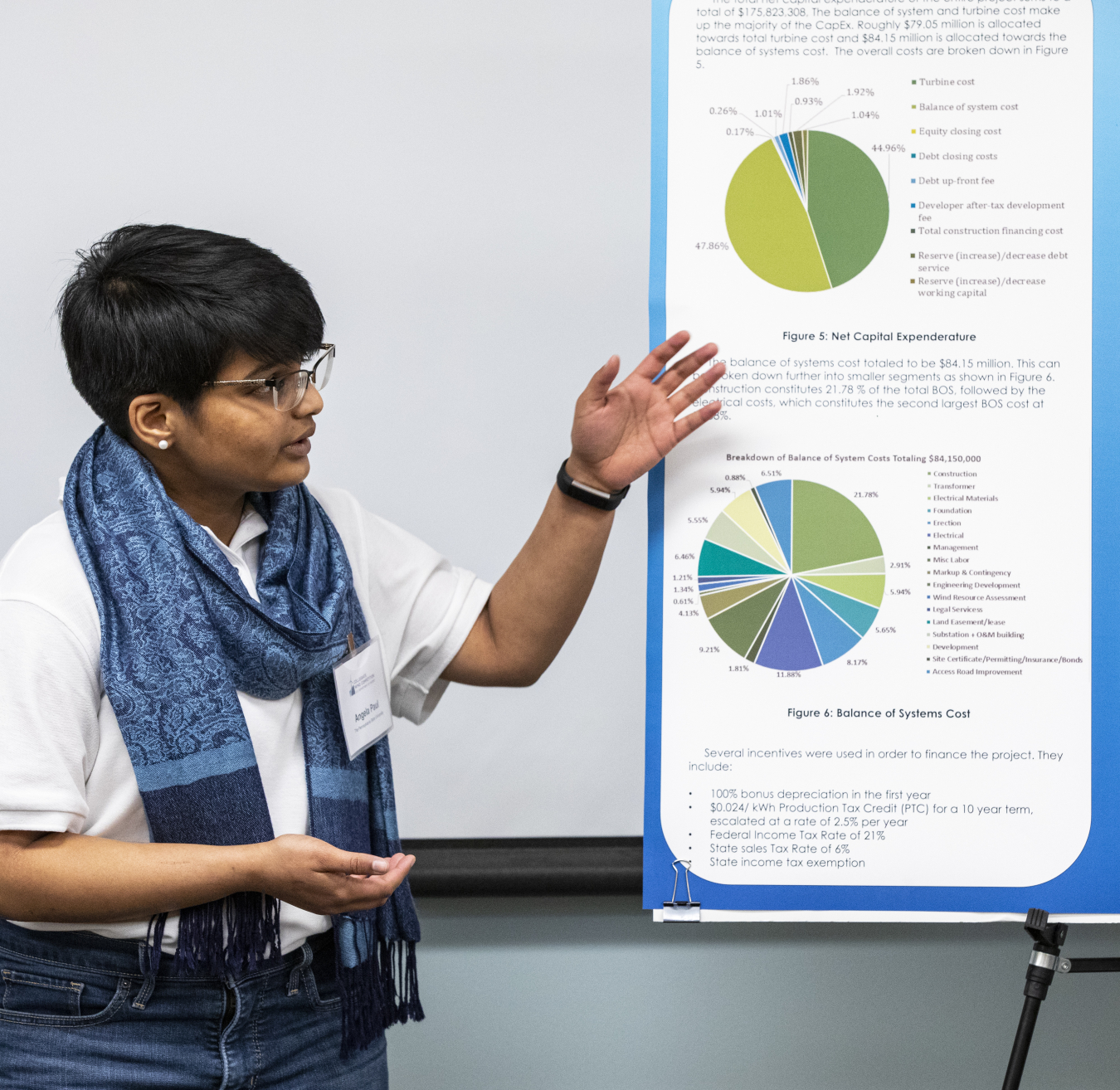 A young woman gestures toward a presentation poster.