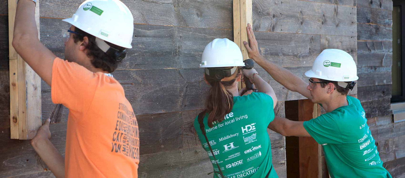 Three student team members in hard hats working on a Solar Decathlon house.