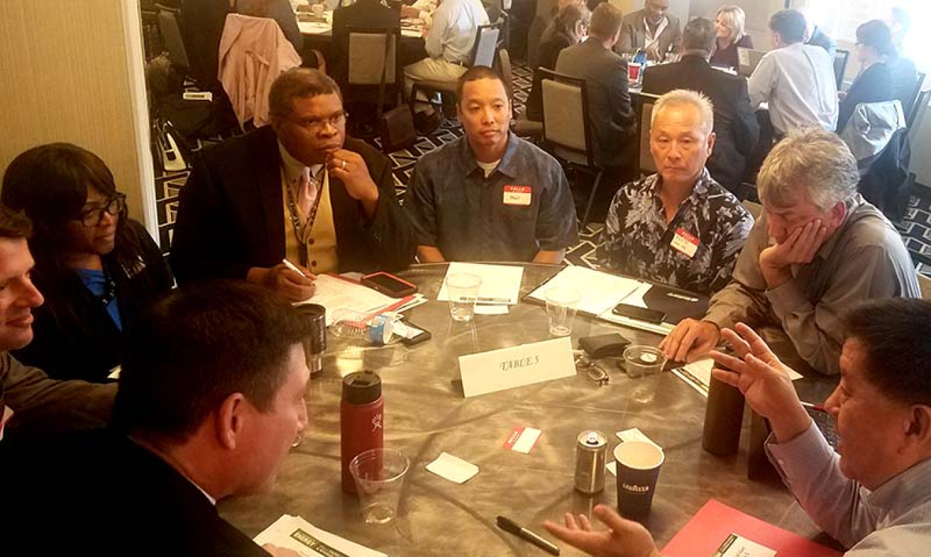 Eight people sitting at a round table listening to one person speak.