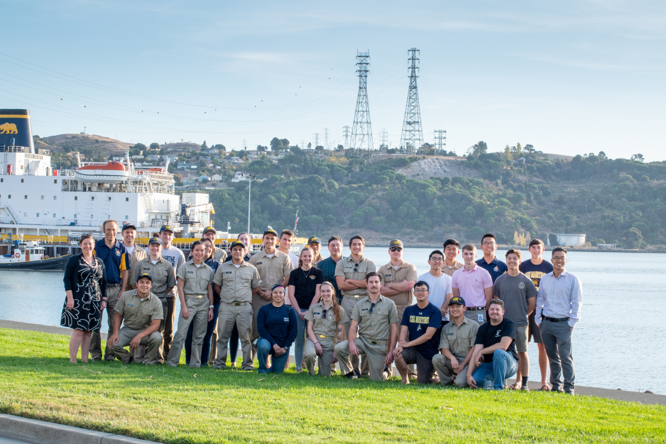 A group of young people, some in uniform, pose in front of a body of water smiling.