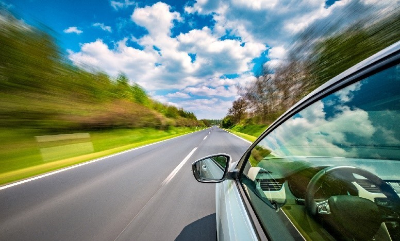 A car driving down a road. a clear sky with lots of cloud above.