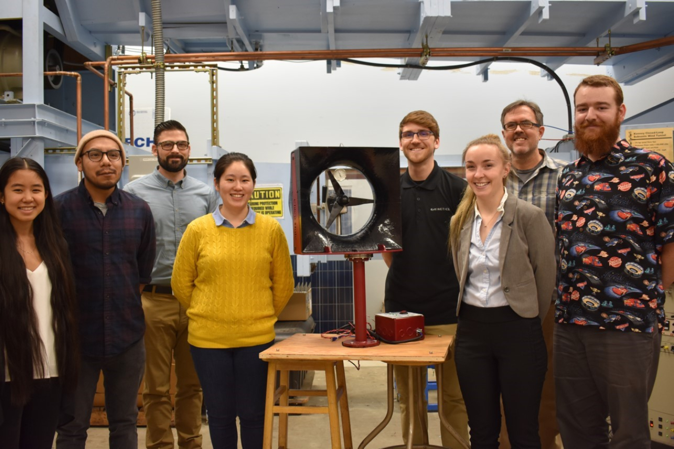 A group of young people stand around a turbine model and smile.