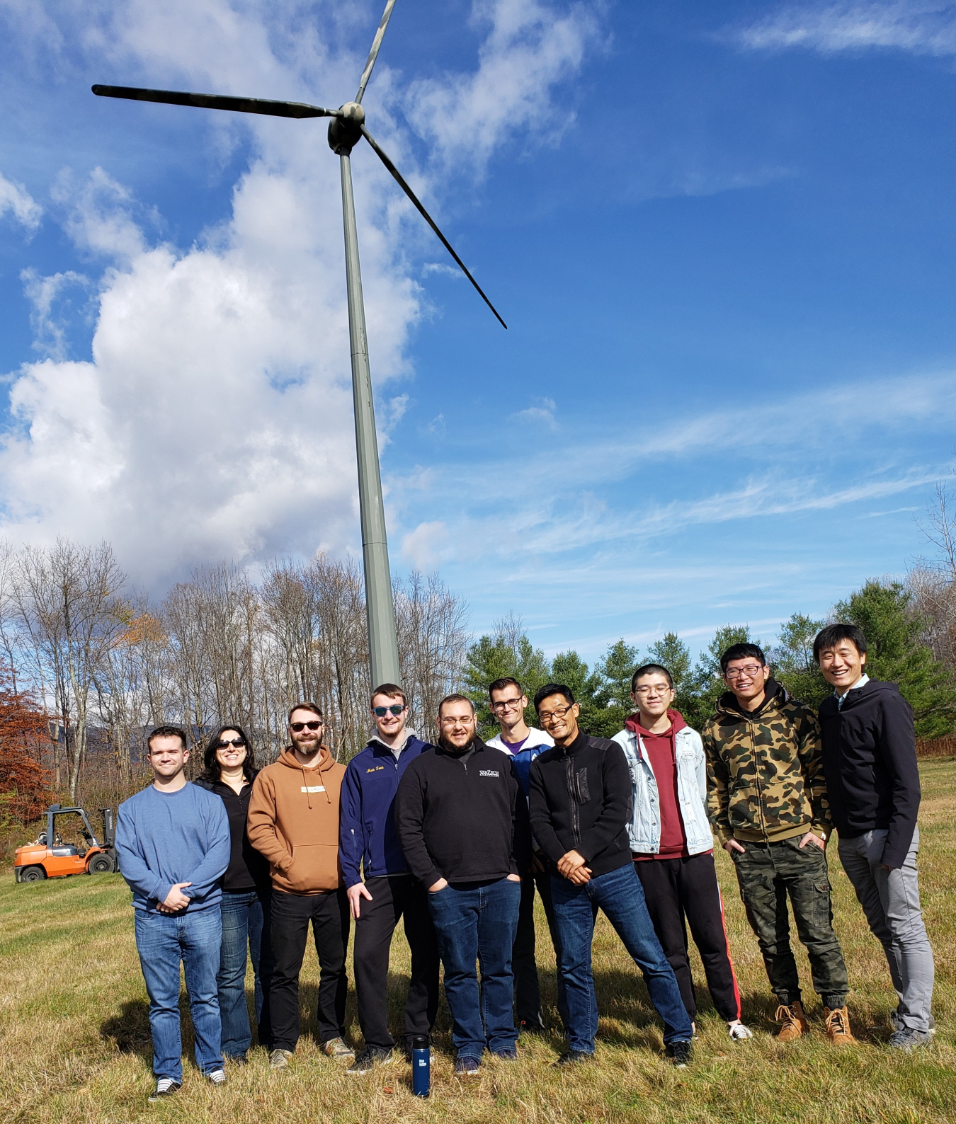 A group of young people stand in front of wind turbines.