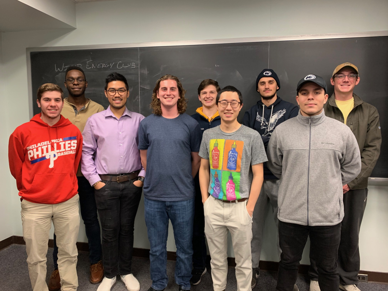 A group of young people stand in front of a chalk board casually smiling.