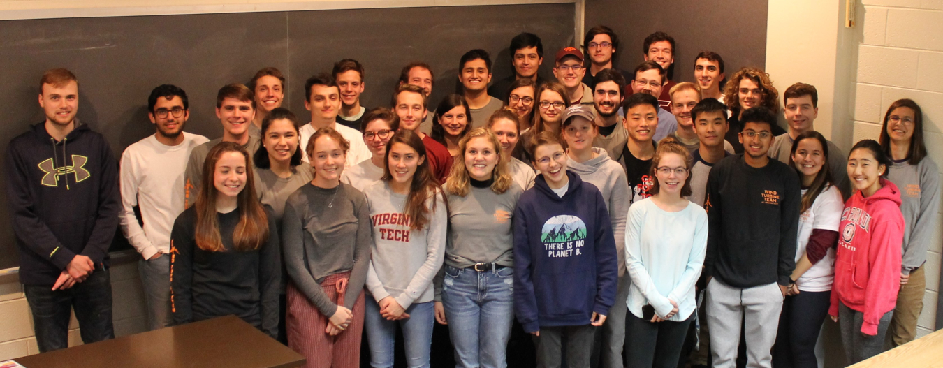 A group of young people stand in front of a chalk board casually smiling. 