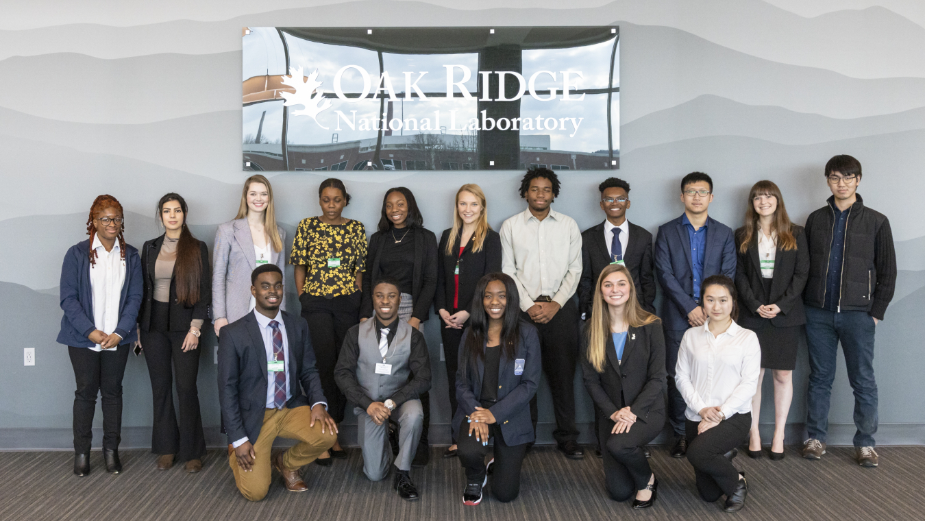 A group of people standing and facing the camera with a sign above them that says Oak Ridge National Laboratory.