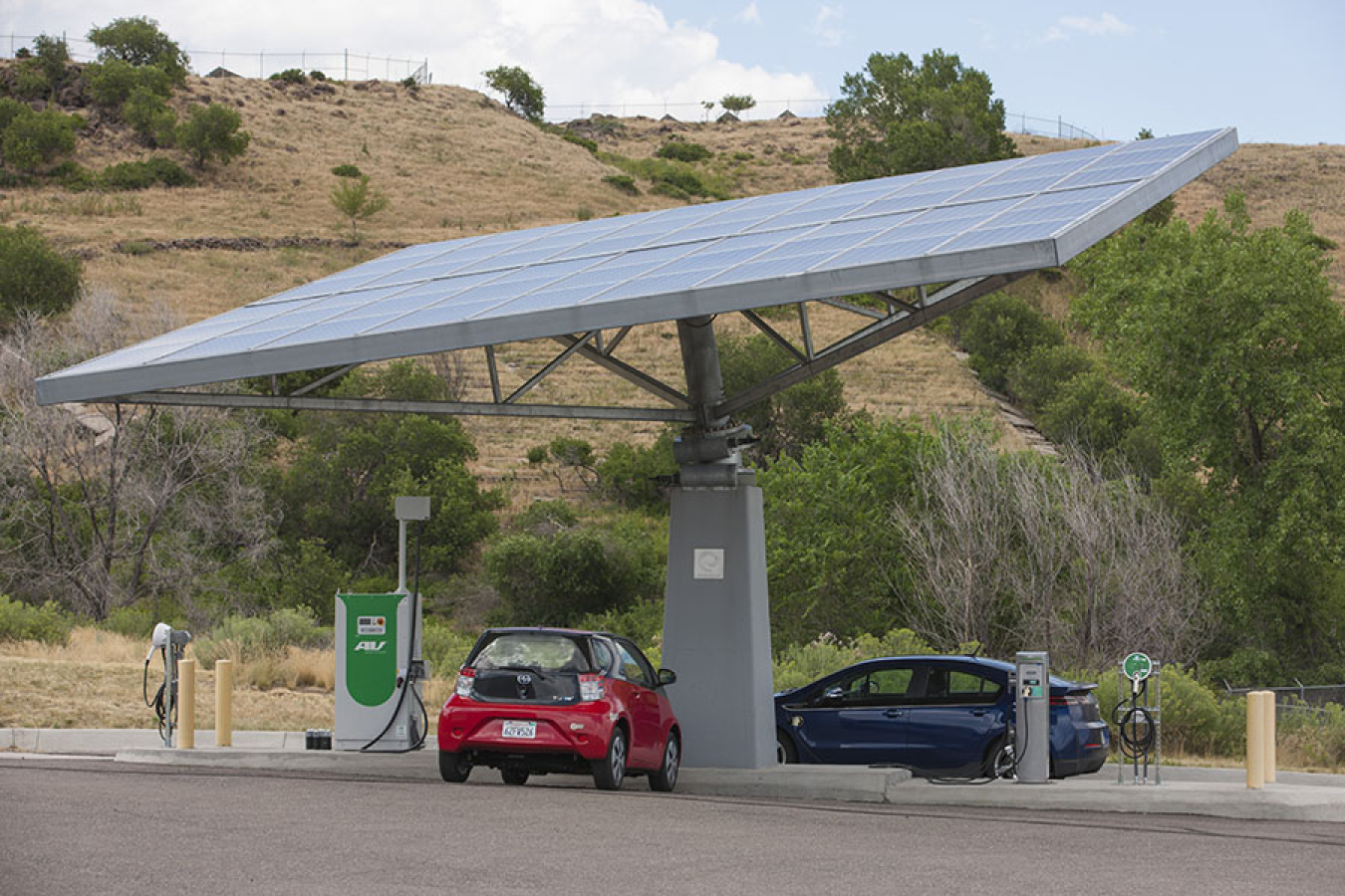 Two electric vehicles at a charging station that has solar panels on the top.