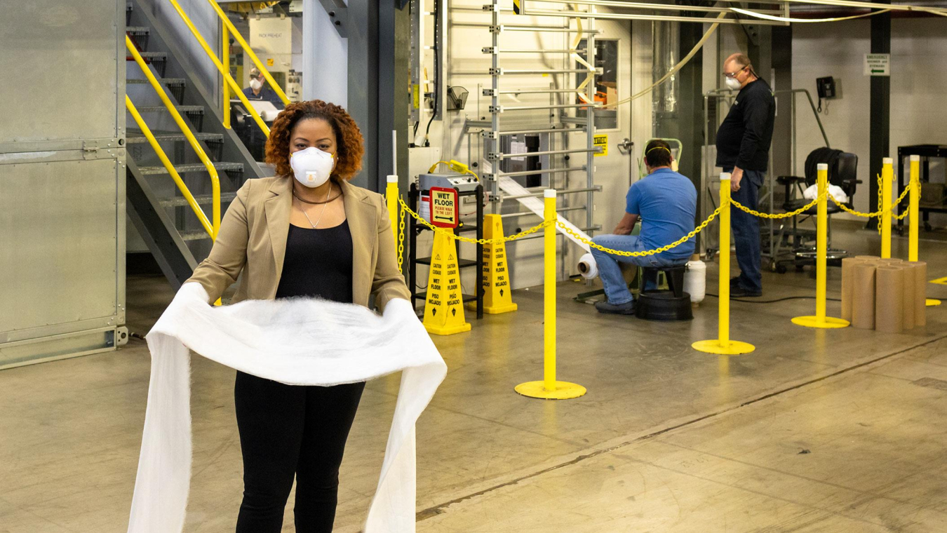 a woman holding some fabric, while wearing a mask