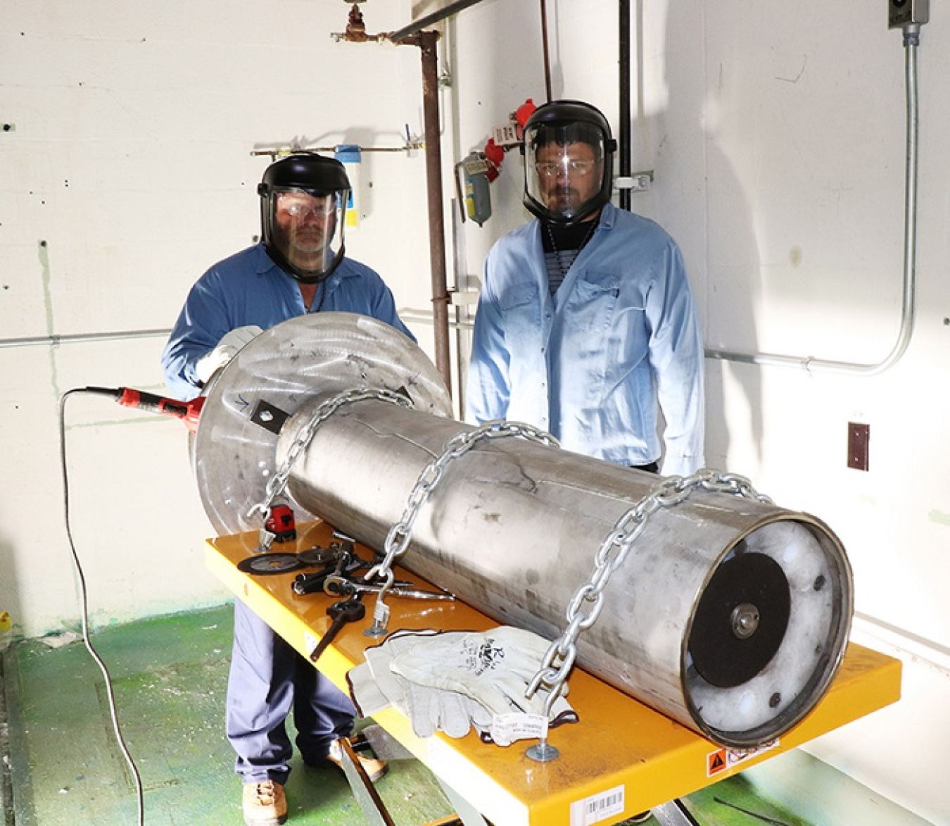 Isotek employees Shane Miles, left, and Ryan Souza stand behind a cutting tool used to help install new remote manipulators in hot cells at Oak Ridge.