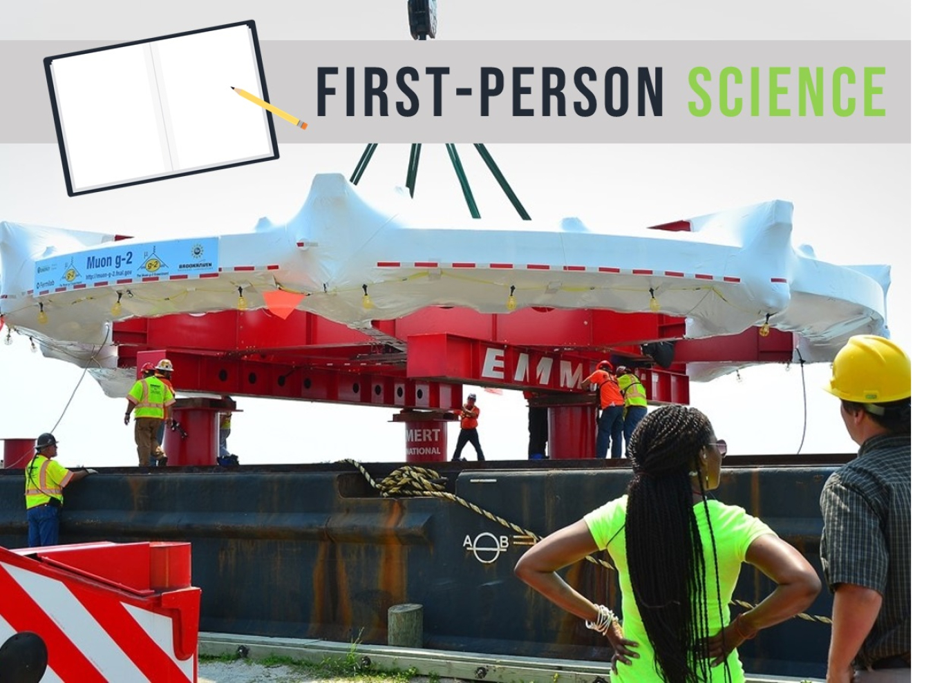 Woman and man standing with their backs to the camera looking at a giant, ring-shaped machine covered in plastic being placed on a large metal platform.