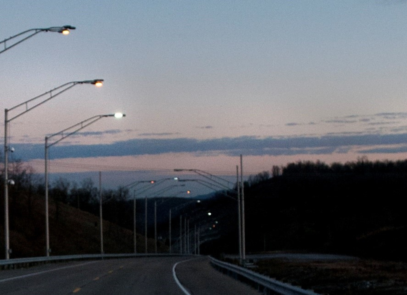 A road at dusk, lined with streetlights.