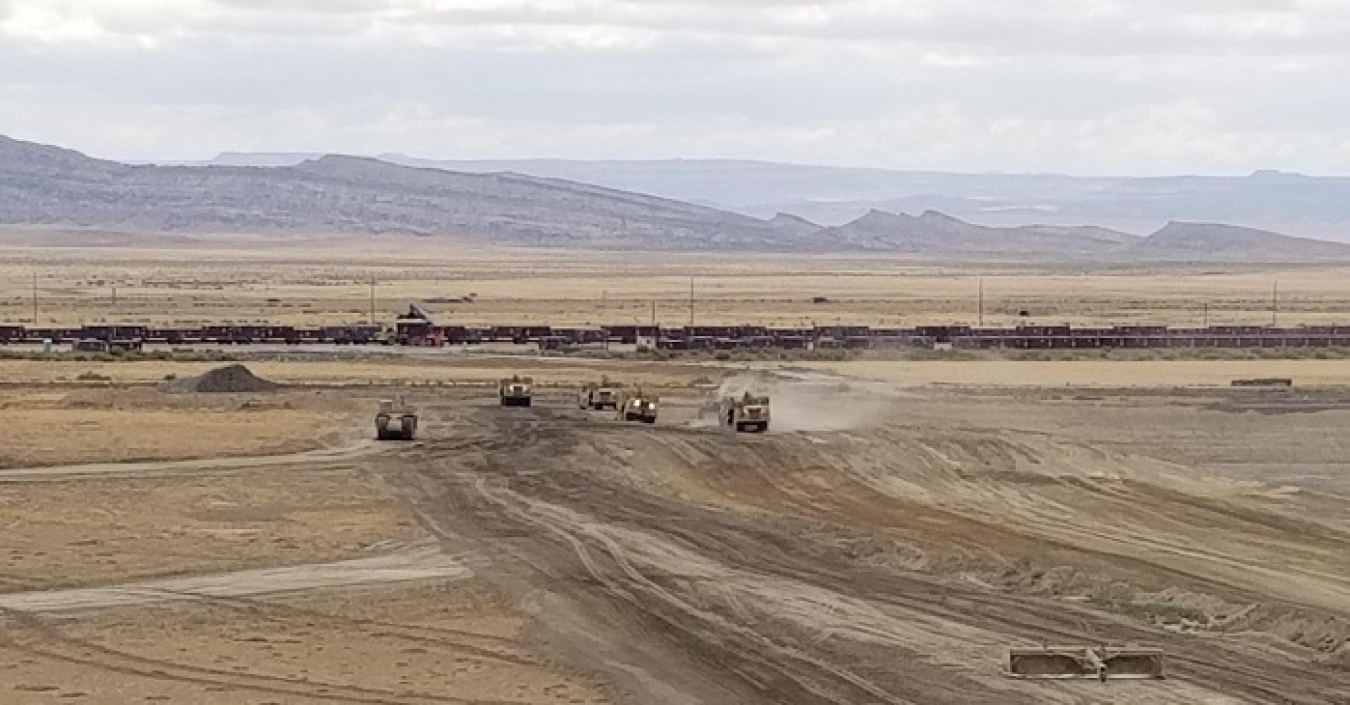 Scrapers excavate a new portion of the disposal cell at Crescent Junction, Utah. In the distance, crews unload containers from the Moab Uranium Mill Tailings Remedial Action Project train.