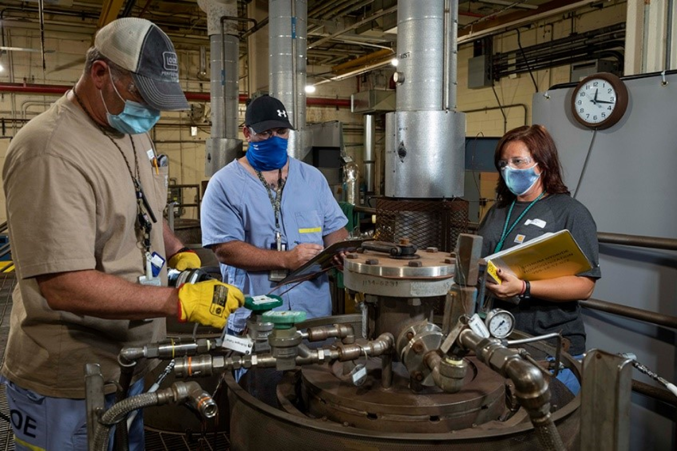 Y-12 chemical operators check a reactor vessel. The homogenization process takes place in the vessel, and several key parameters are checked and recorded hourly.