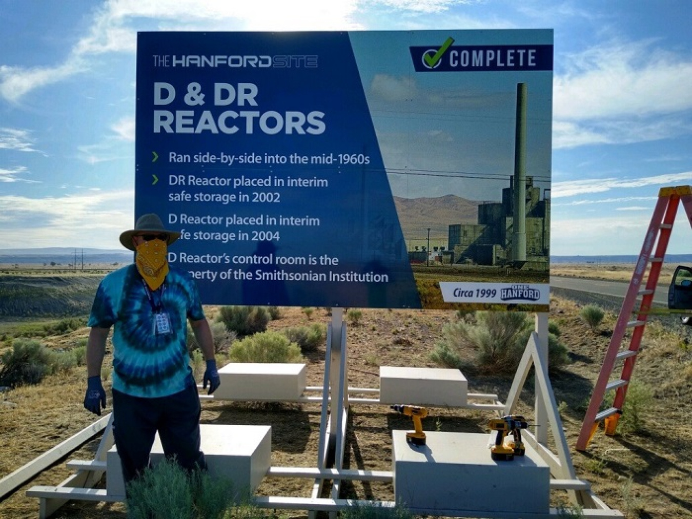 John Doty, sign painter for EM Richland Operations Office contractor Mission Support Alliance, stands in front of a landmark sign commemorating the cleanup of 135 waste sites.