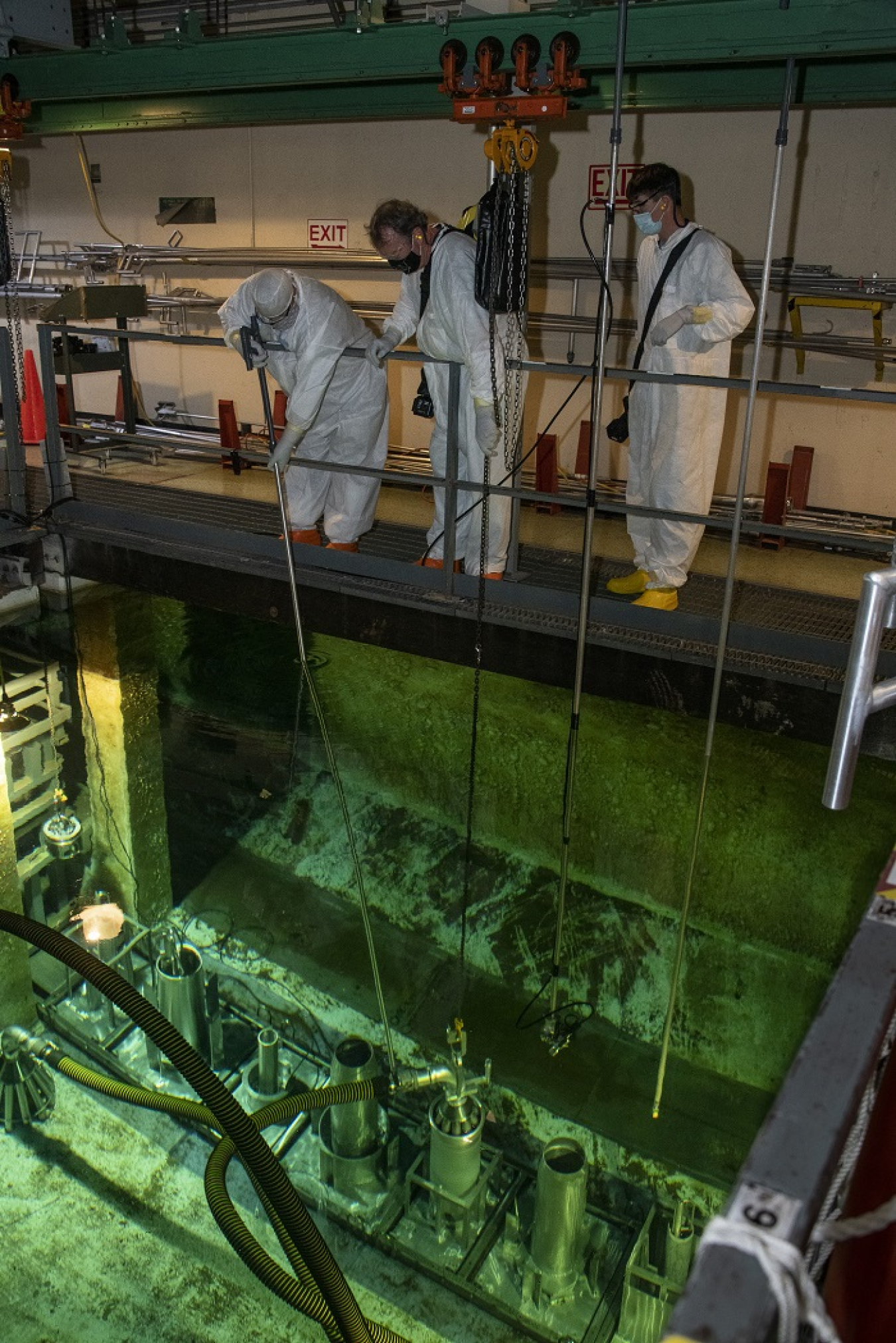 Savannah River Nuclear Solutions operators Thomas Dill, Jack Phillips, and Carl Cato use a long-handled tool to position an underwater vacuum on top of a High Flux Isotope Reactor core in L Basin at the Savannah River Site.