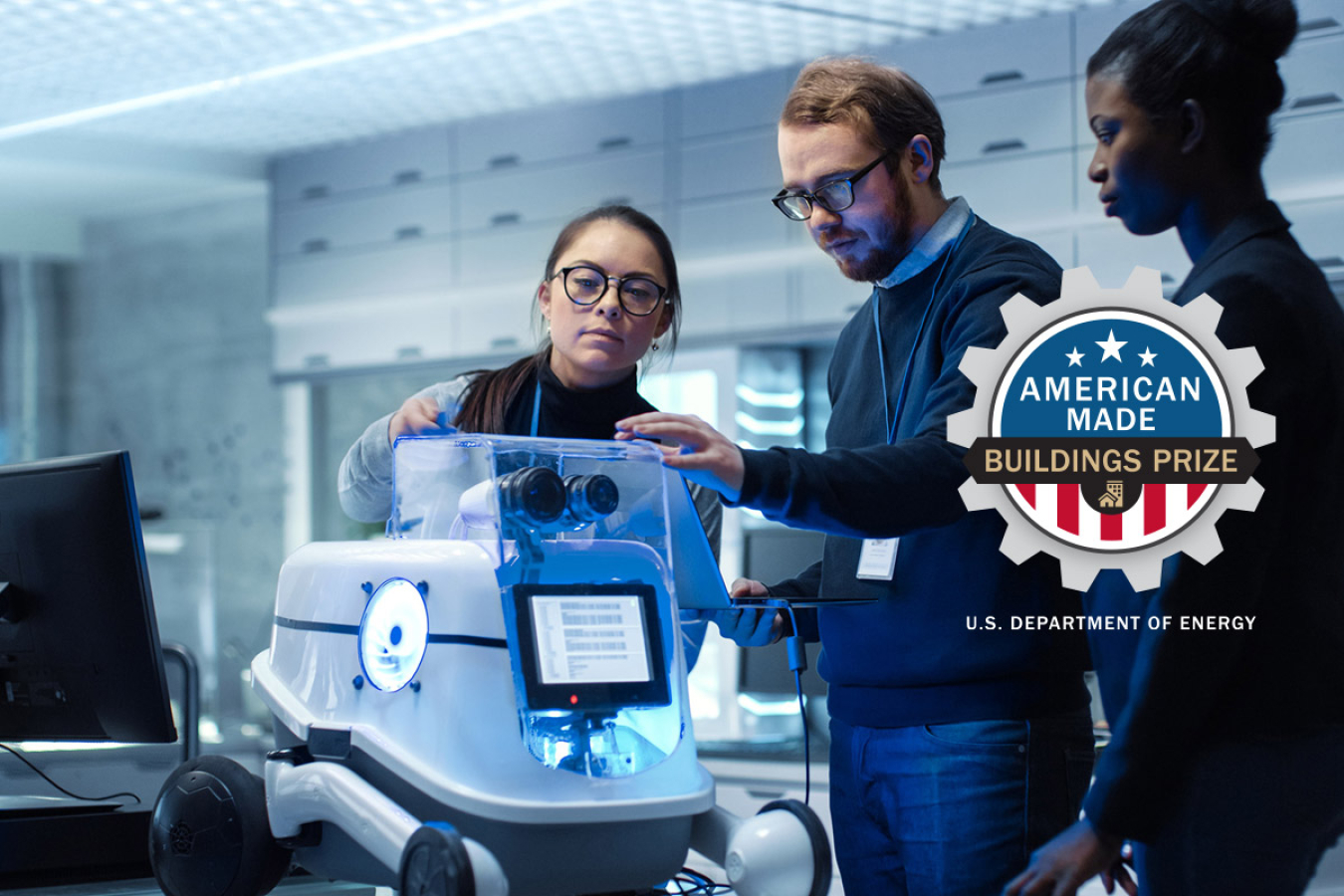 Photo of three people looking at a piece of machinery, with the American-Made Buildings Prize logo.