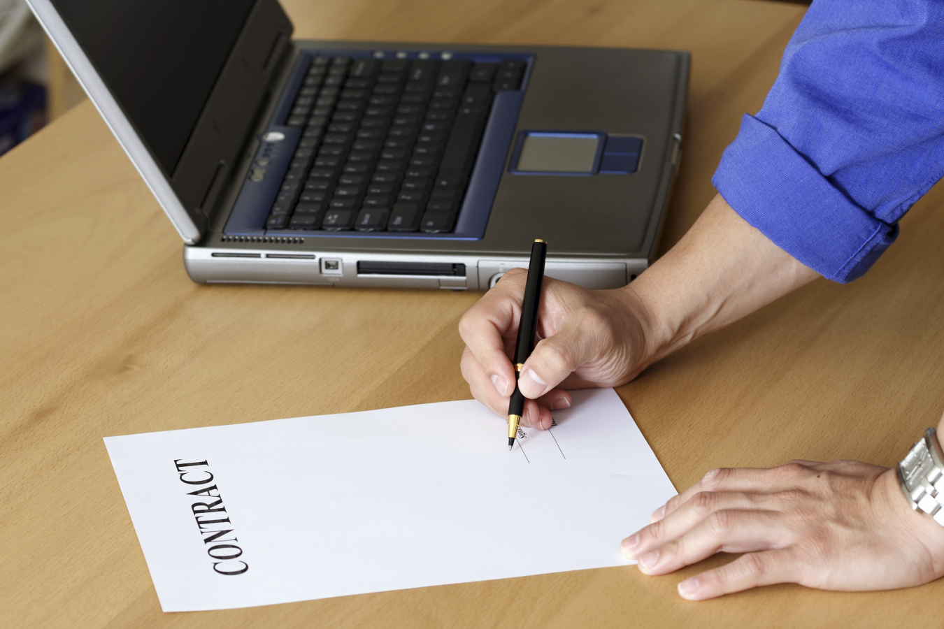 Person writing a contract with a computer.