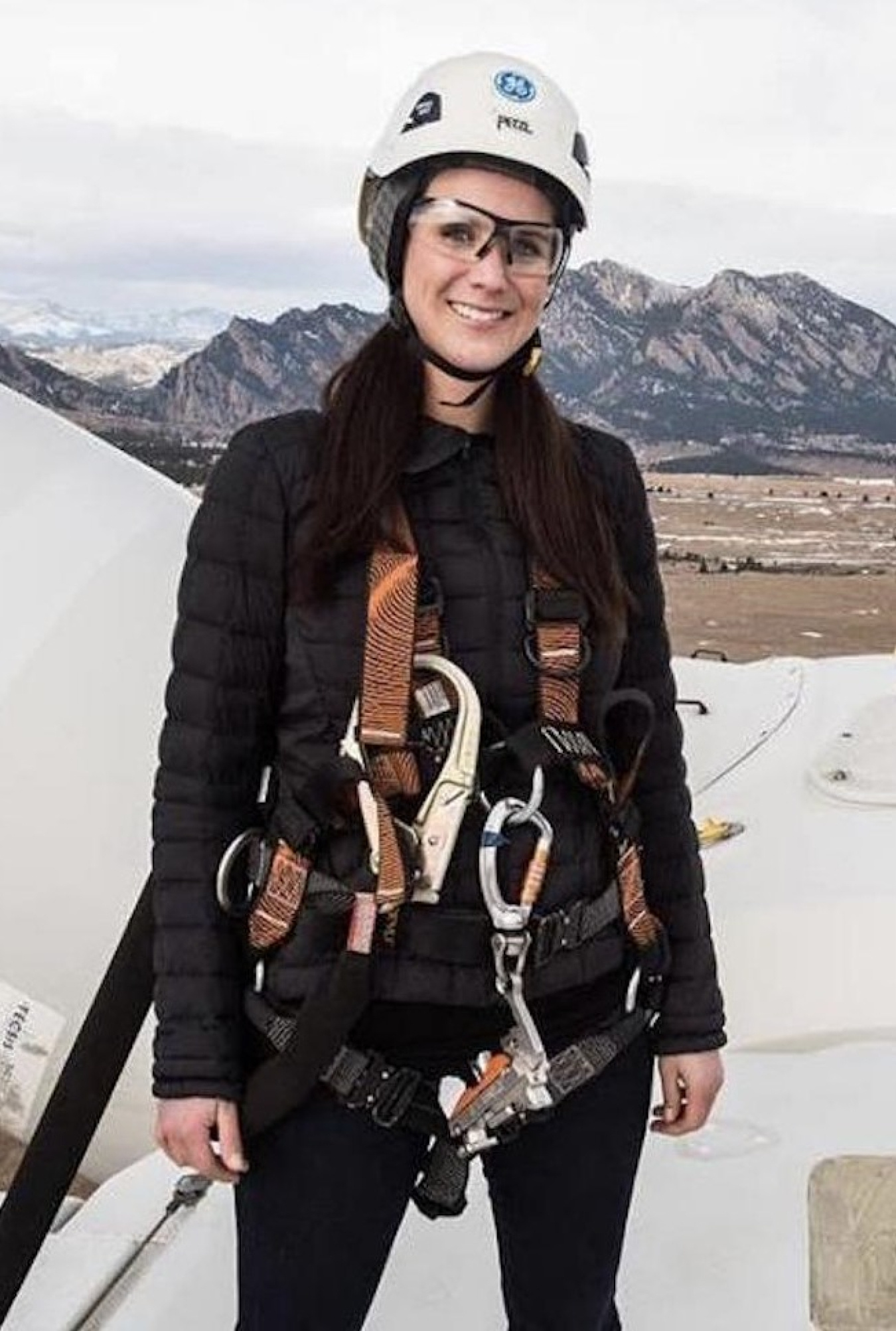 Picture of a female in climbing gear with mountains in the background.