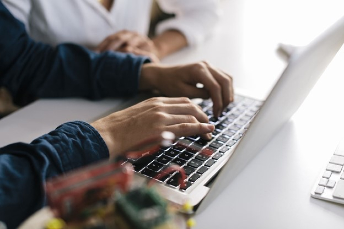 two people at a table with an open laptop and one person's hands on the keyboard.