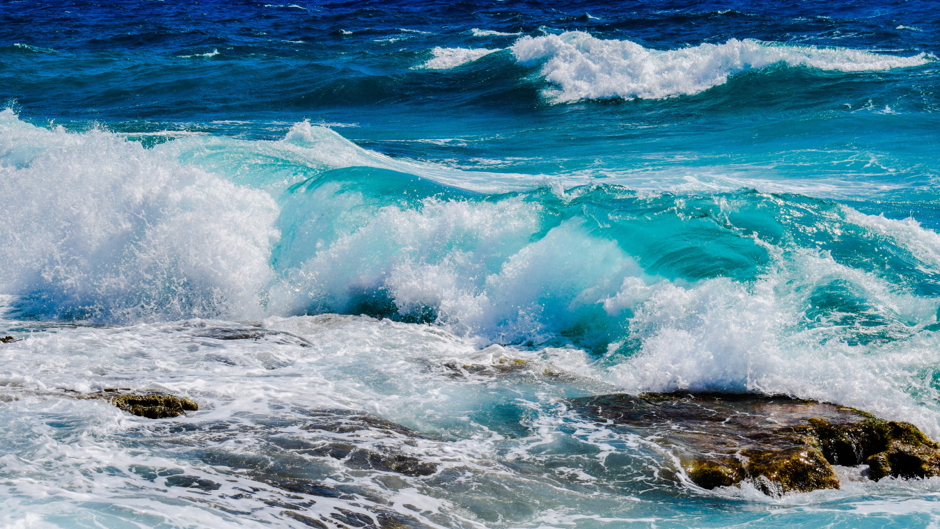 Photo of the ocean, waves are crashing in the foreground on rocks.