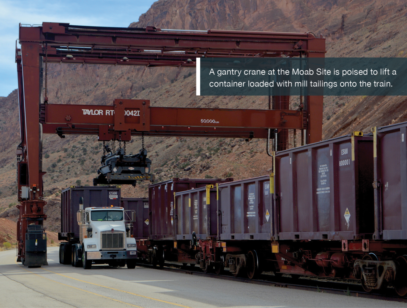 A gantry crane at the Moab Site is poised to lift a container loaded with mill tailings onto the train.