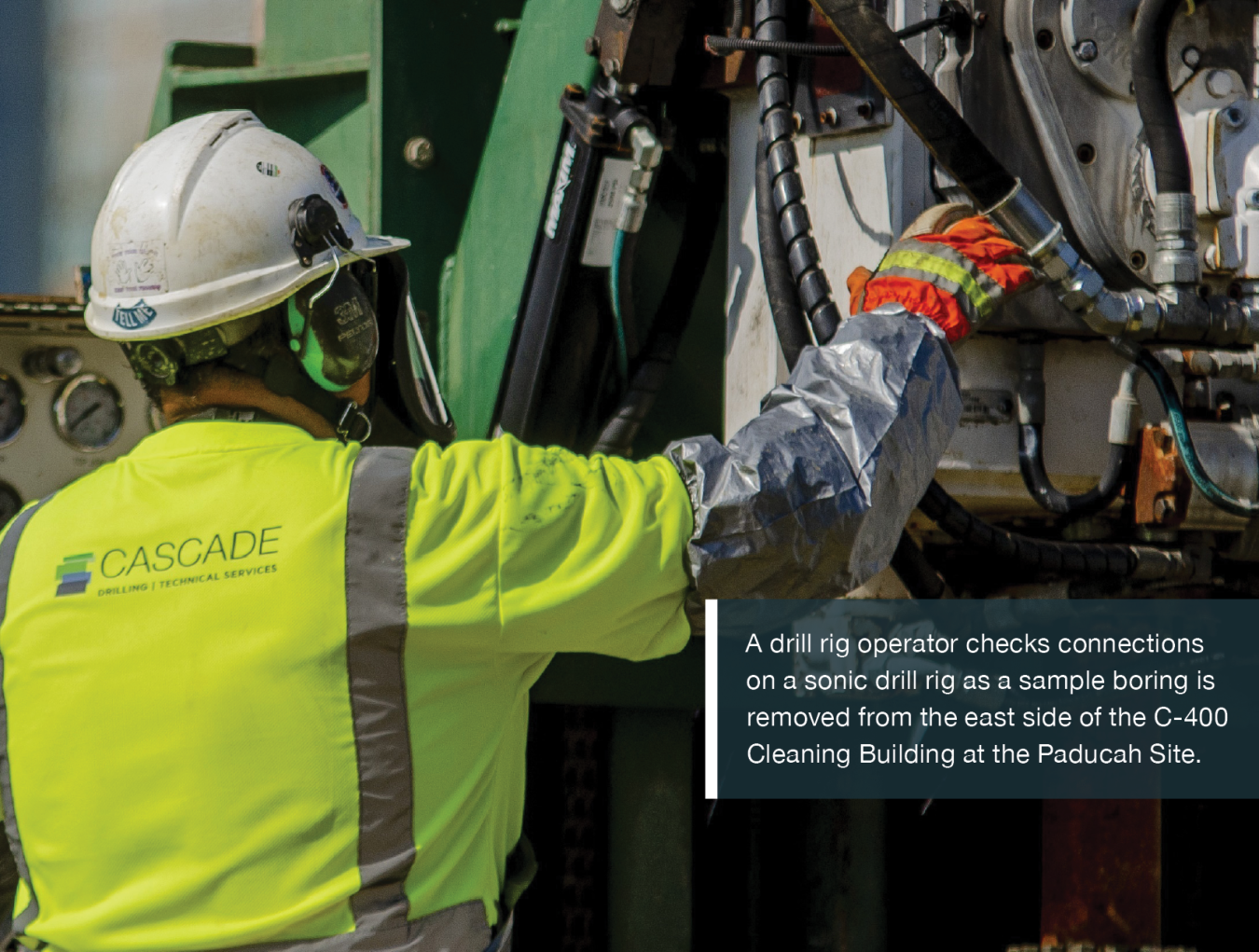 A drill rig operator checks connections on a sonic drill rig as a sample boring is removed from the east side of the C-400 Cleaning Building at the Paducah Site.