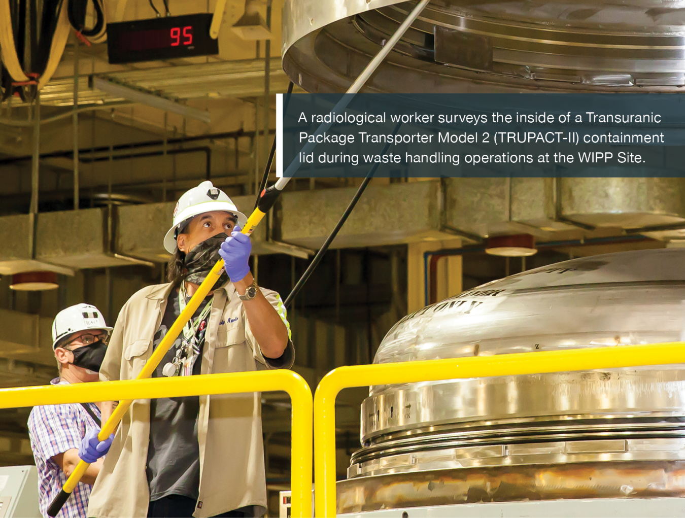 A radiological worker surveys the inside of a Transuranic Package Transporter Model 2 (TRUPACT-II) containment lid during waste handling operations at the WIPP Site.