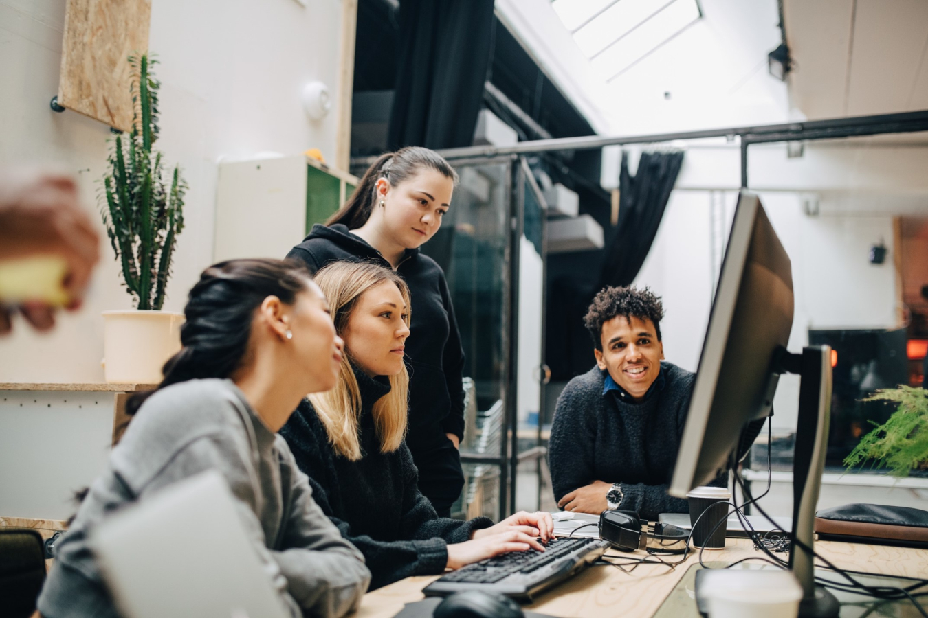 four young professionals huddled in front of a computer screen.