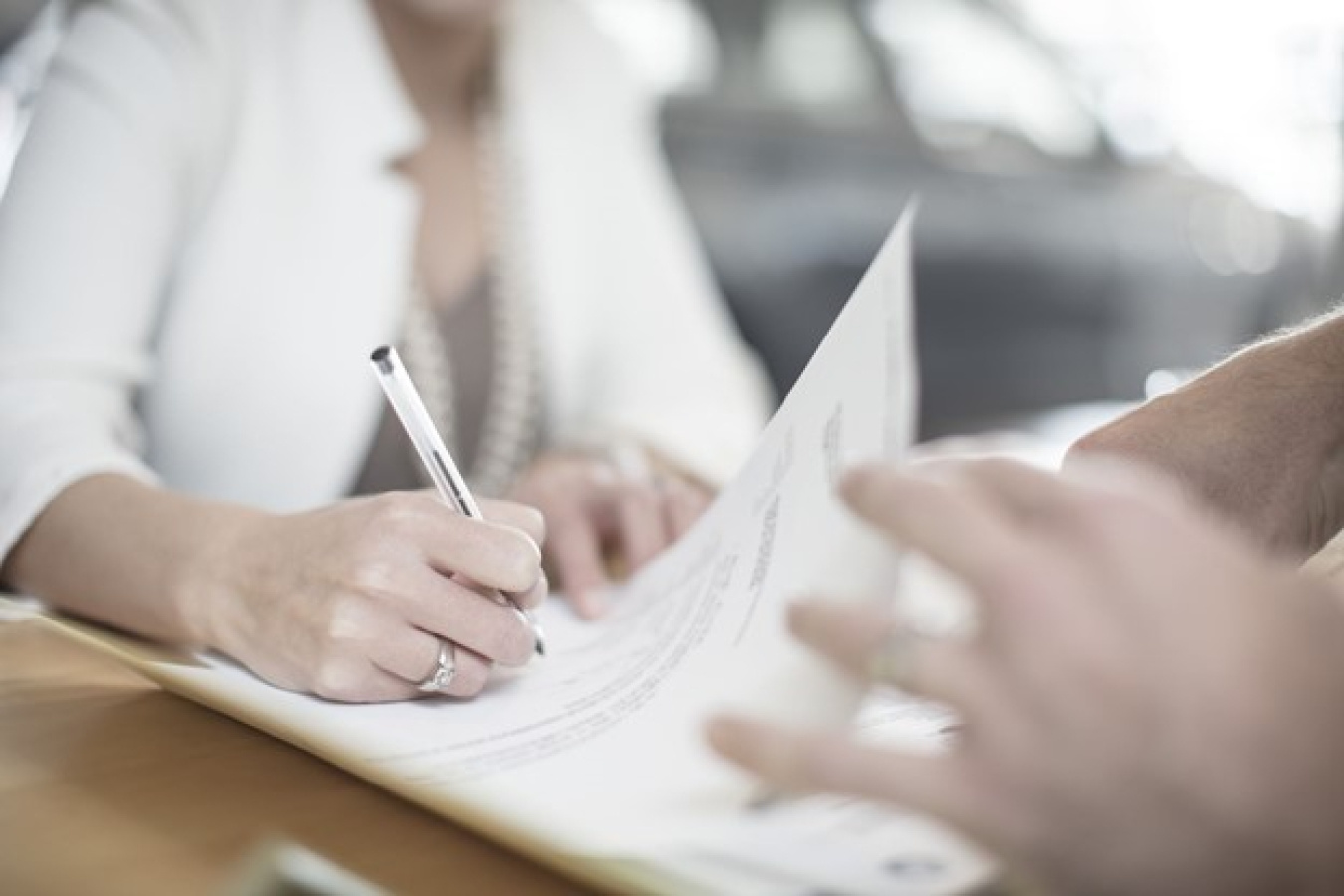 A shot of one person signing a document and another holding the paper.