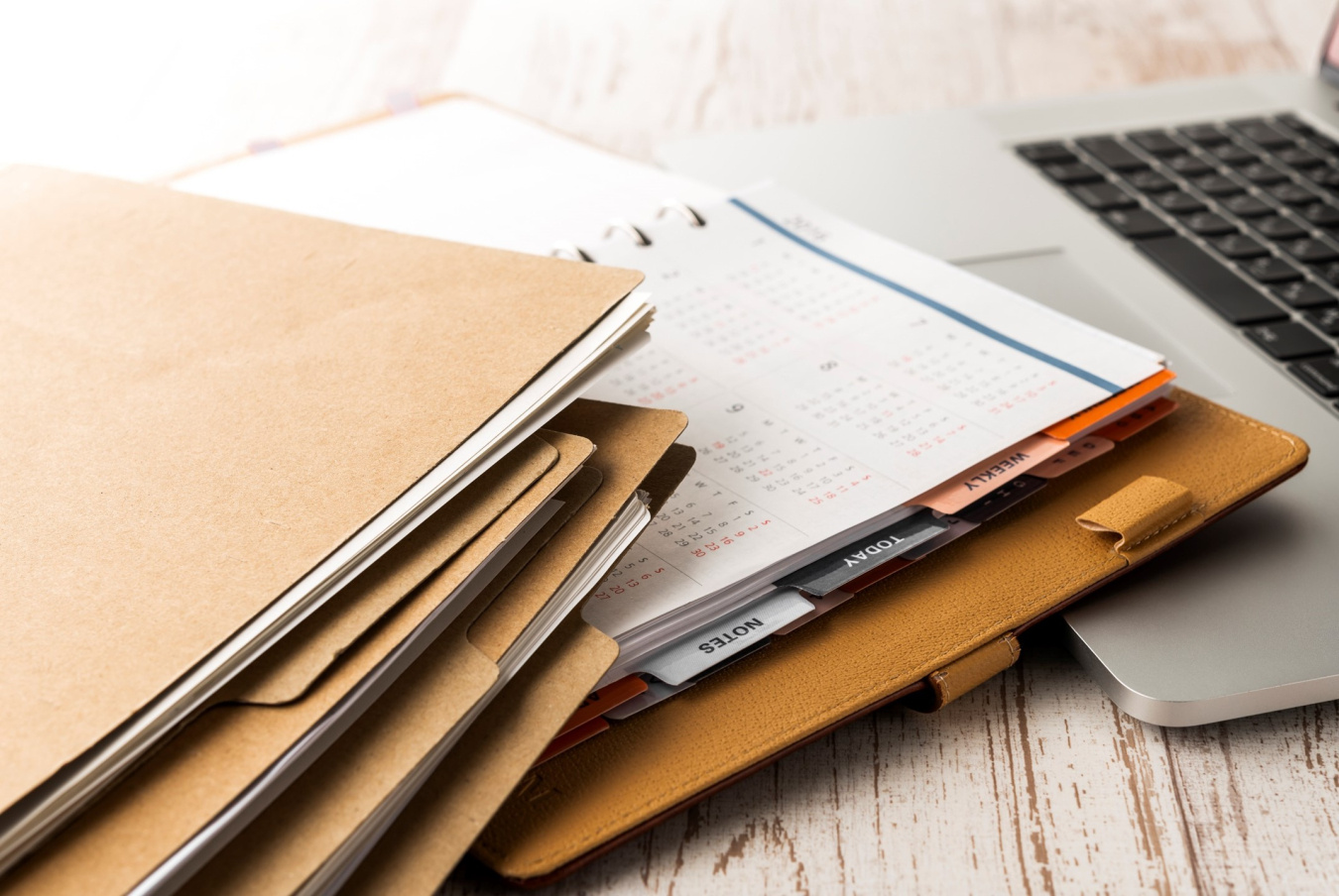 Brown file folders and an open organizer and laptop sit on a table. 