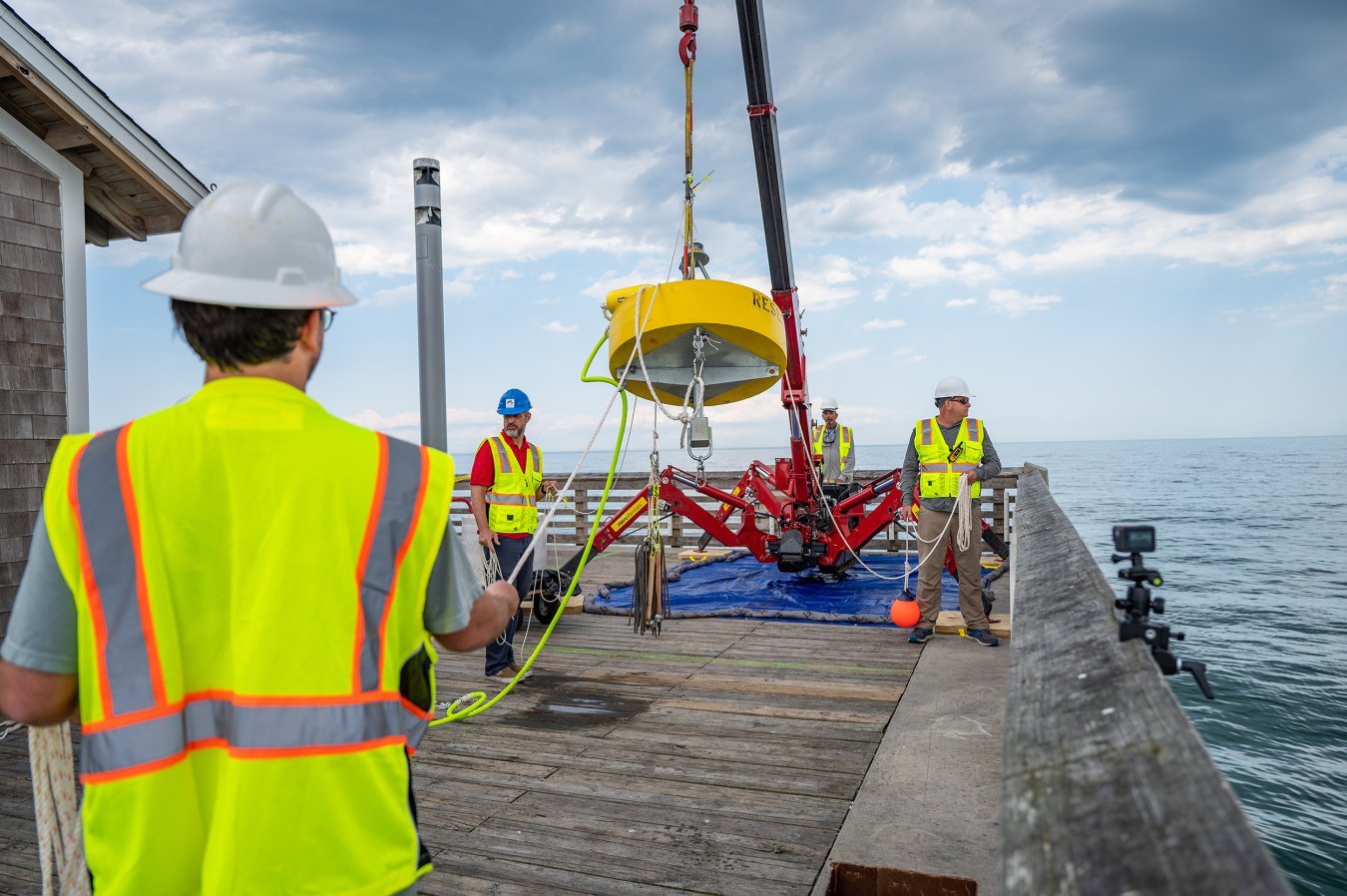 Workers stand on a dock deploying marine energy equipment.