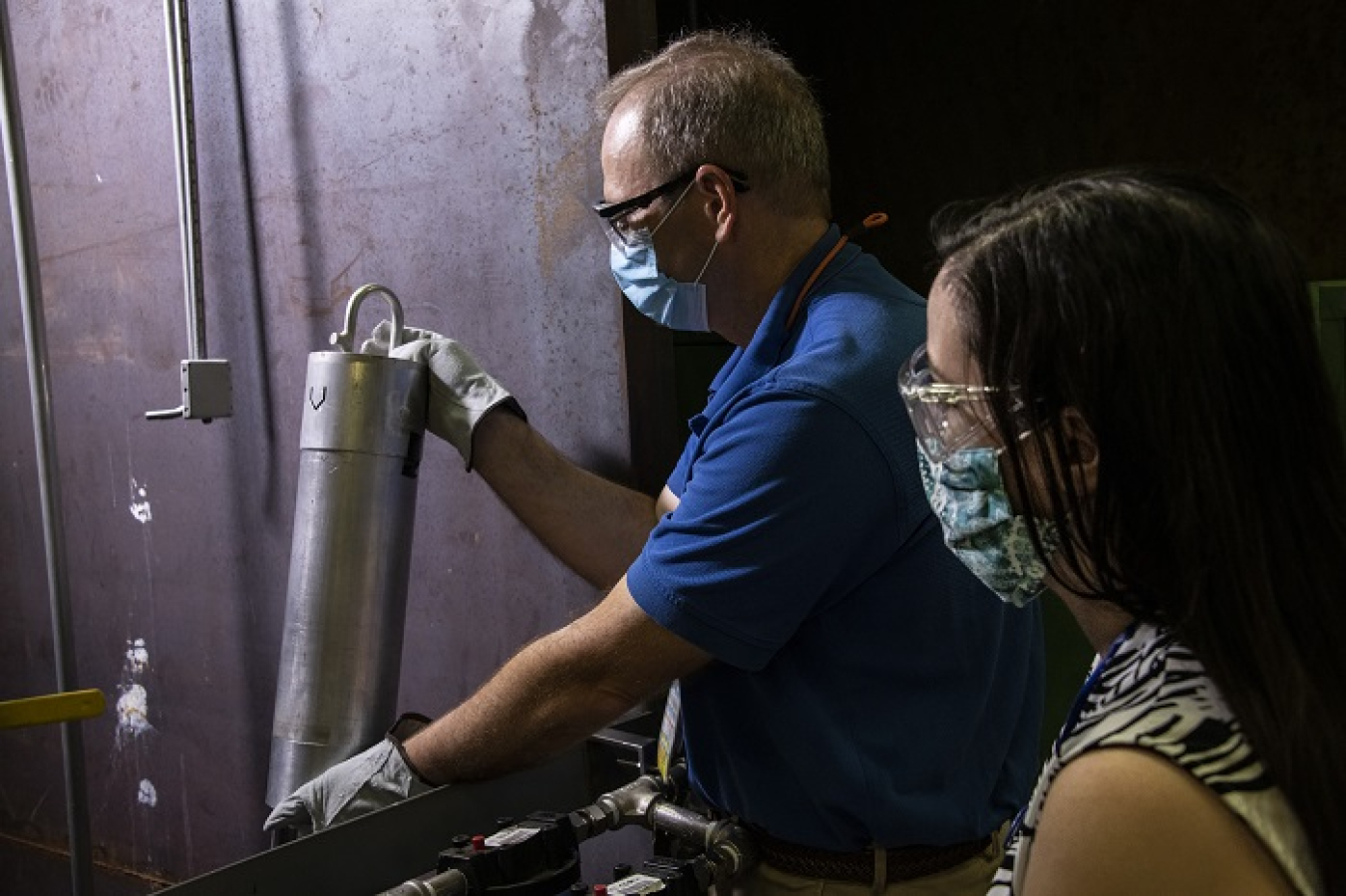 Savannah River Nuclear Solutions and Savannah River National Laboratory (SRNL) developed a mock-up to test underwater cameras and accompanying long-handled tools to perform examinations of spent nuclear fuel bundles in a basin at the Savannah River Site. Here SRNL employee Kevin Counts holds a small section of a test bundle against an underwater camera as SRNL employee Lisa Ward looks on.
