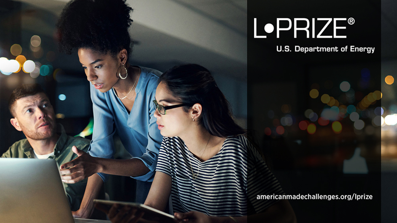 Three people clustered around a computer in discussion, with blurred colored lights in the background and the L-Prize logo and URL