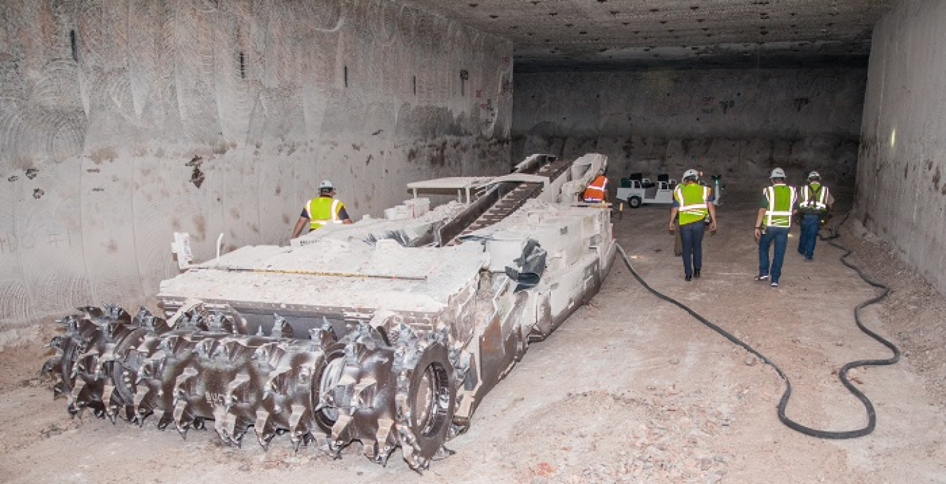 An electric-powered continuous miner machine is shown at rest in Panel 8 at the Waste Isolation Pilot Plant after cutting the floor to its final height. The machine, using its movable head and sharp teeth, can mine 8 to 10 tons per minute.