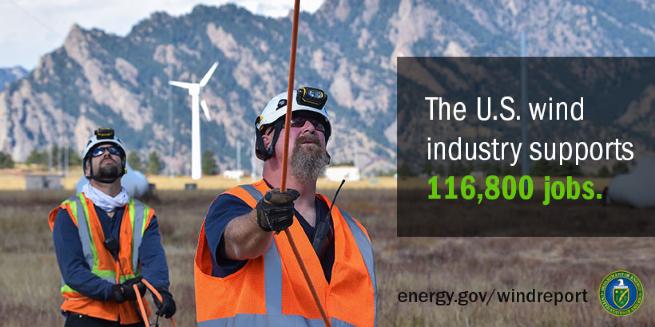 Mountains and wind turbines in the background, with wind workers looking up in the foreground.