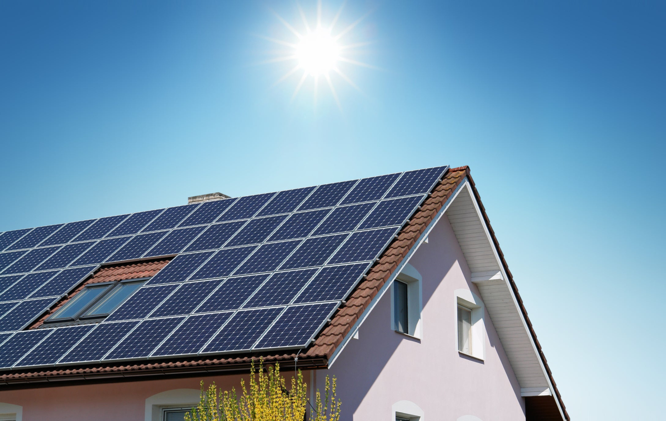 A house with rooftop solar panels and the sun shining above it. 