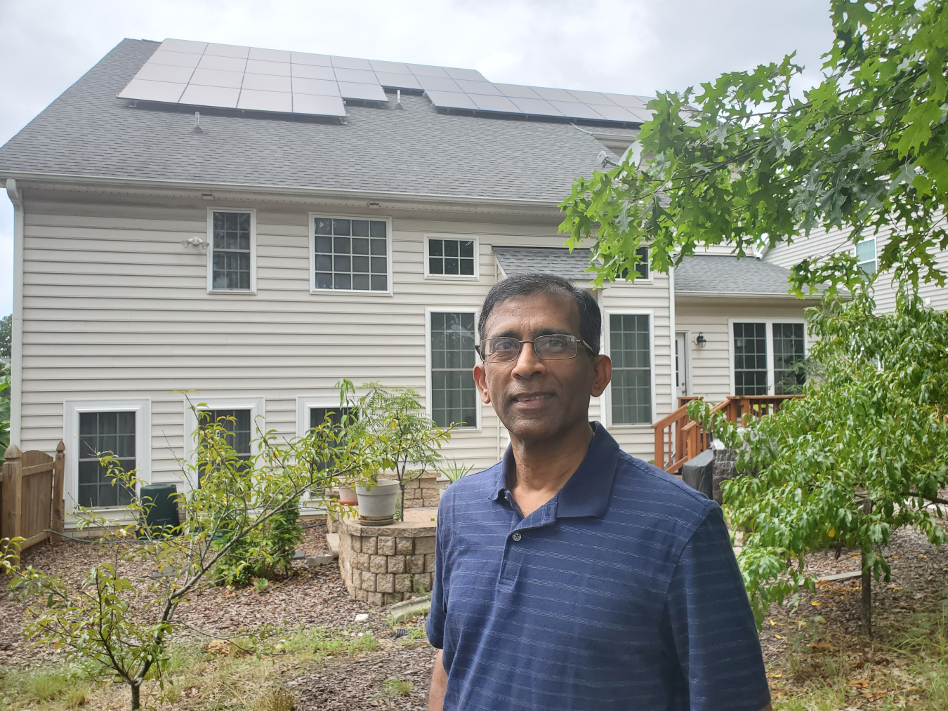 A person standing in front of a house with solar panels on the roof