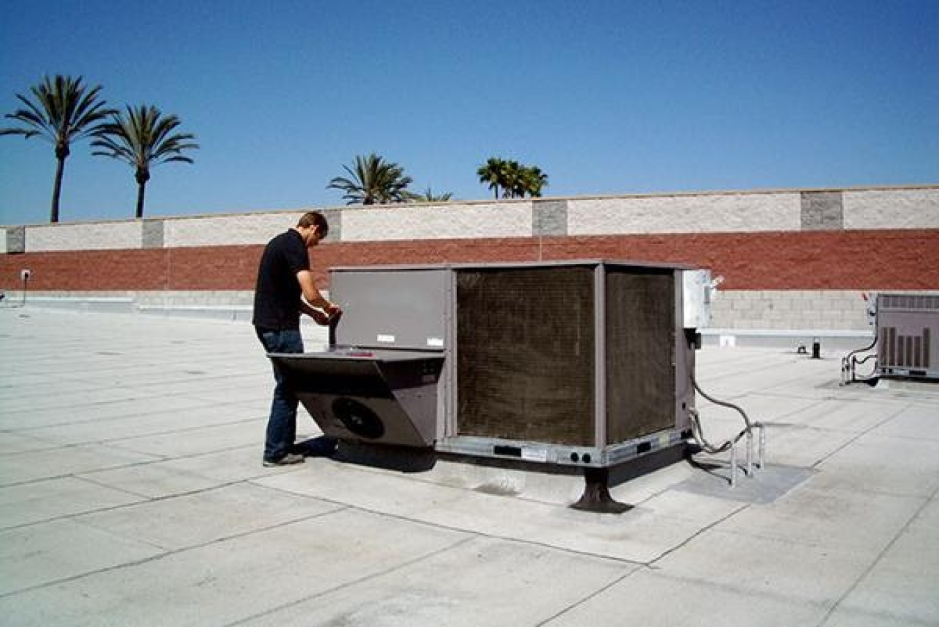 A man on the roof of a commercial building working on a rooftop HVAC unit.