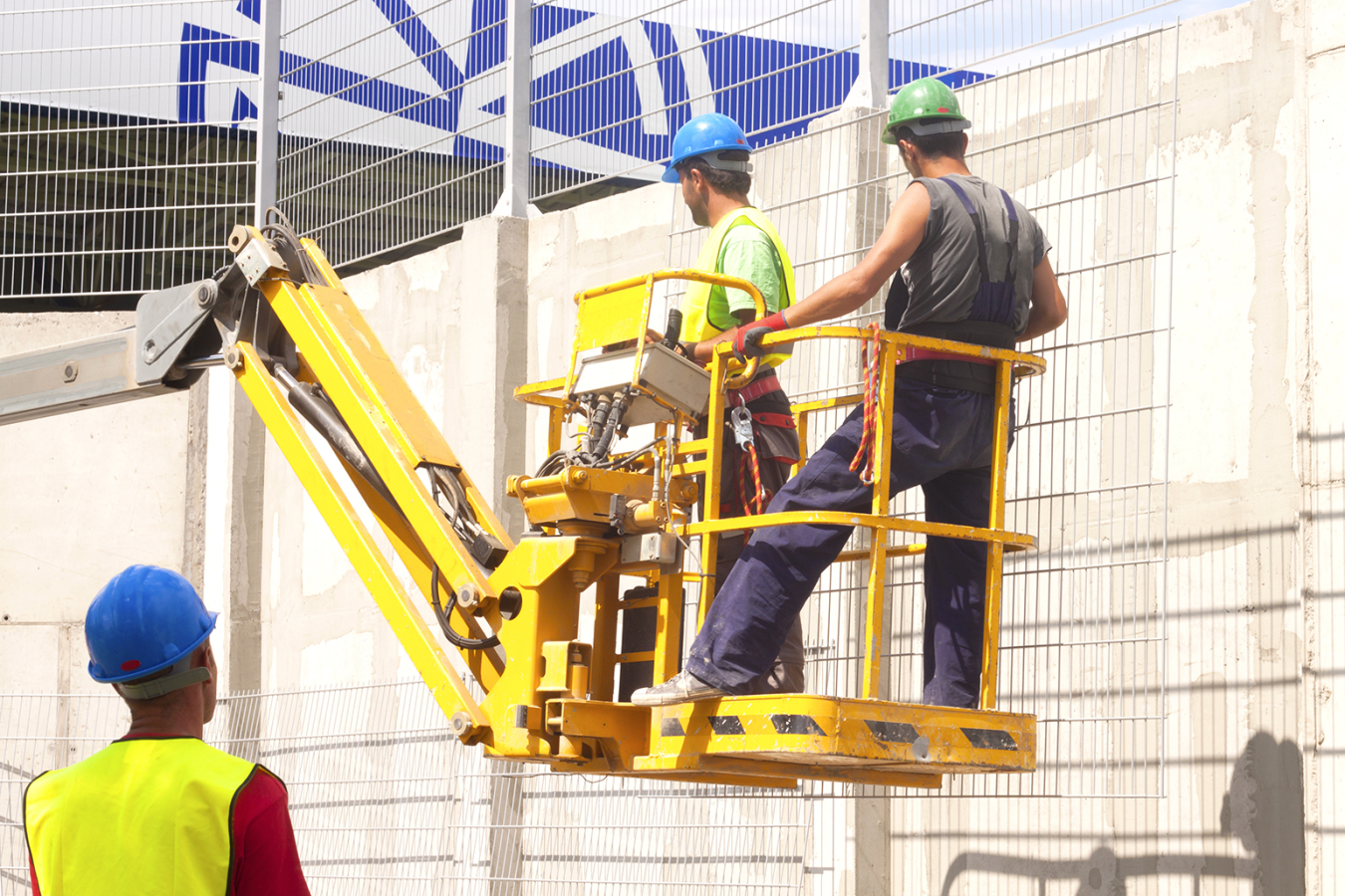 Construction workers using a hoisting machine to inspect wall.