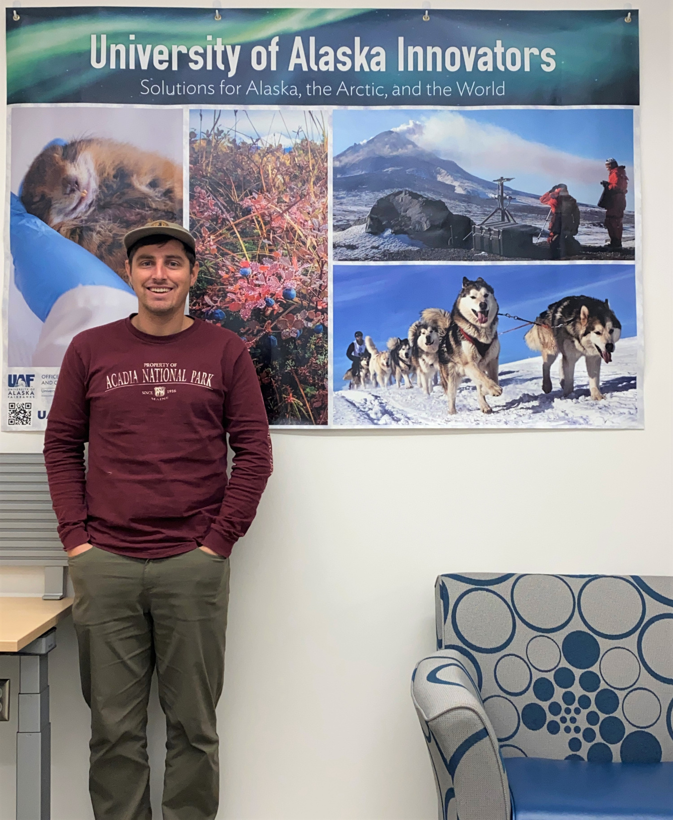 Arctic Innovator Chris Woodruff stands in front of a University of Alaska poster.