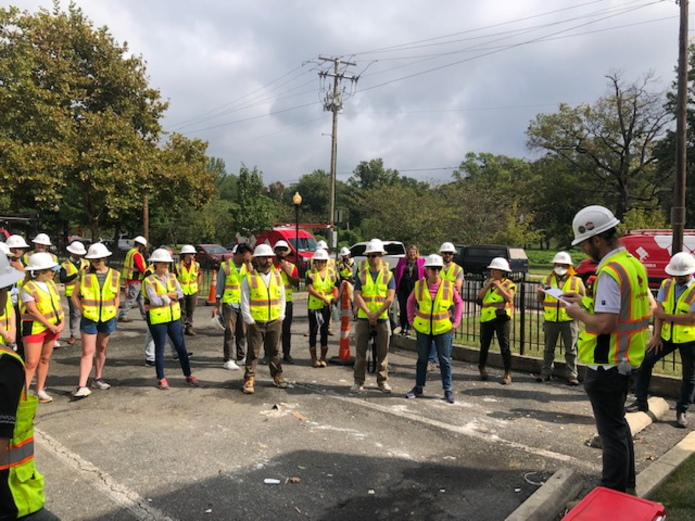 Team members, wearing hard hats and safety vests, receive a briefing from their crew leader before beginning a community solar installation in Washington, DC.