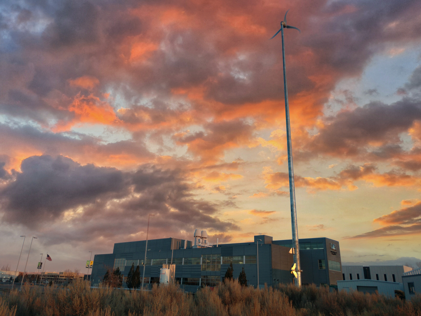 Small wind turbine stands beside a building at sunset.